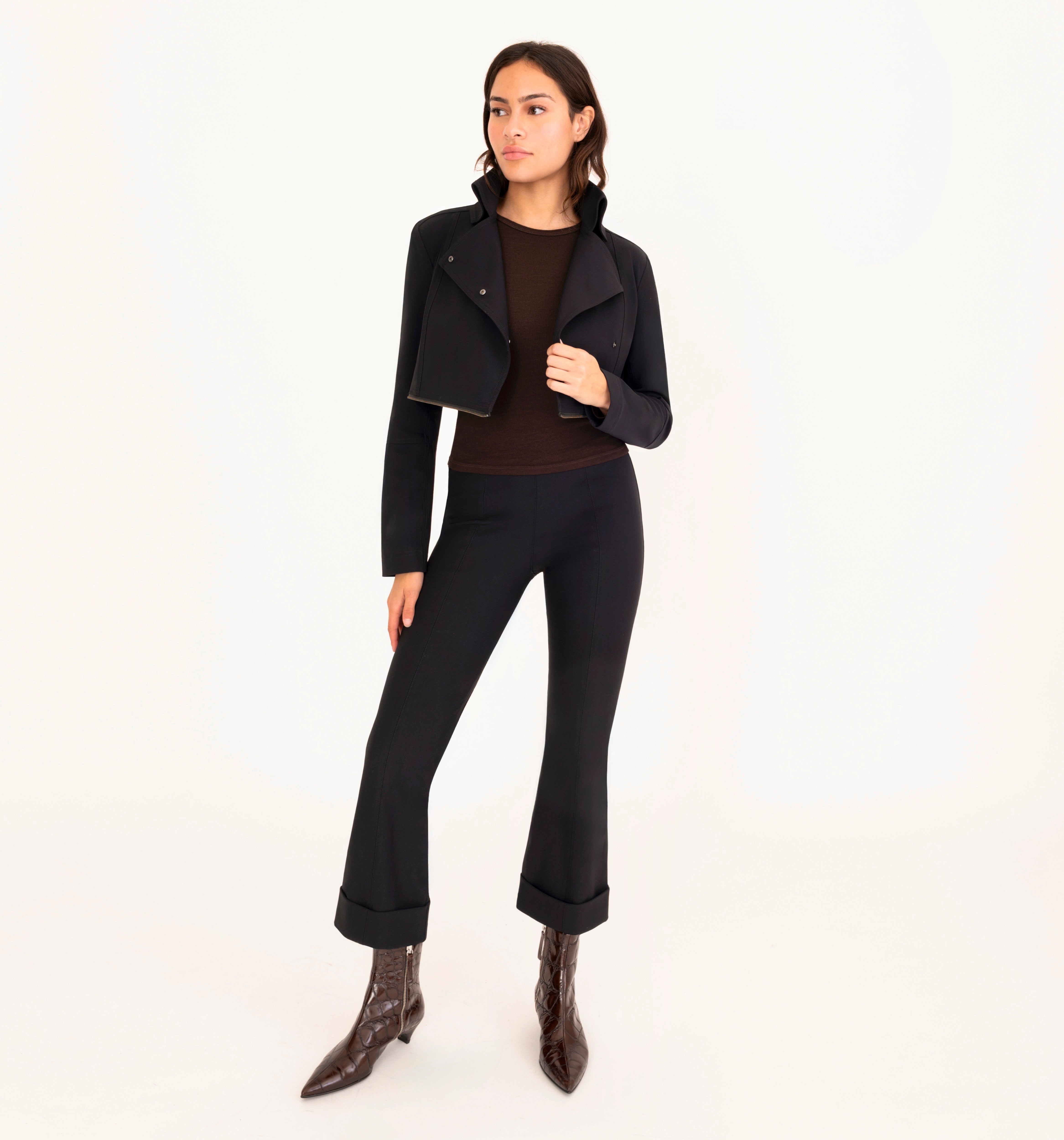 Woman wearing a black jacket, black pants, and brown boots on a white background