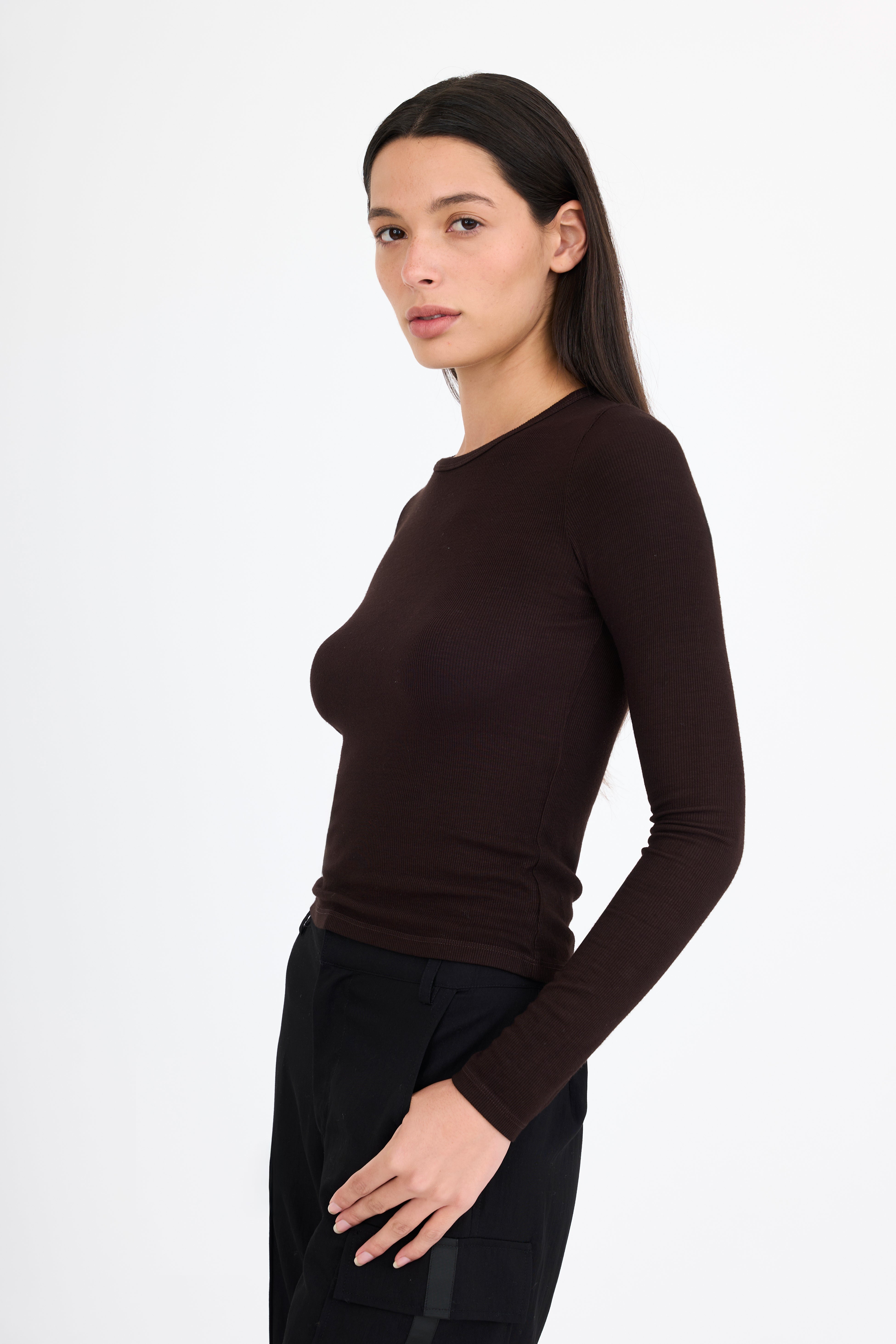 Woman wearing a brown long-sleeve t-shirt and black pants on a white background