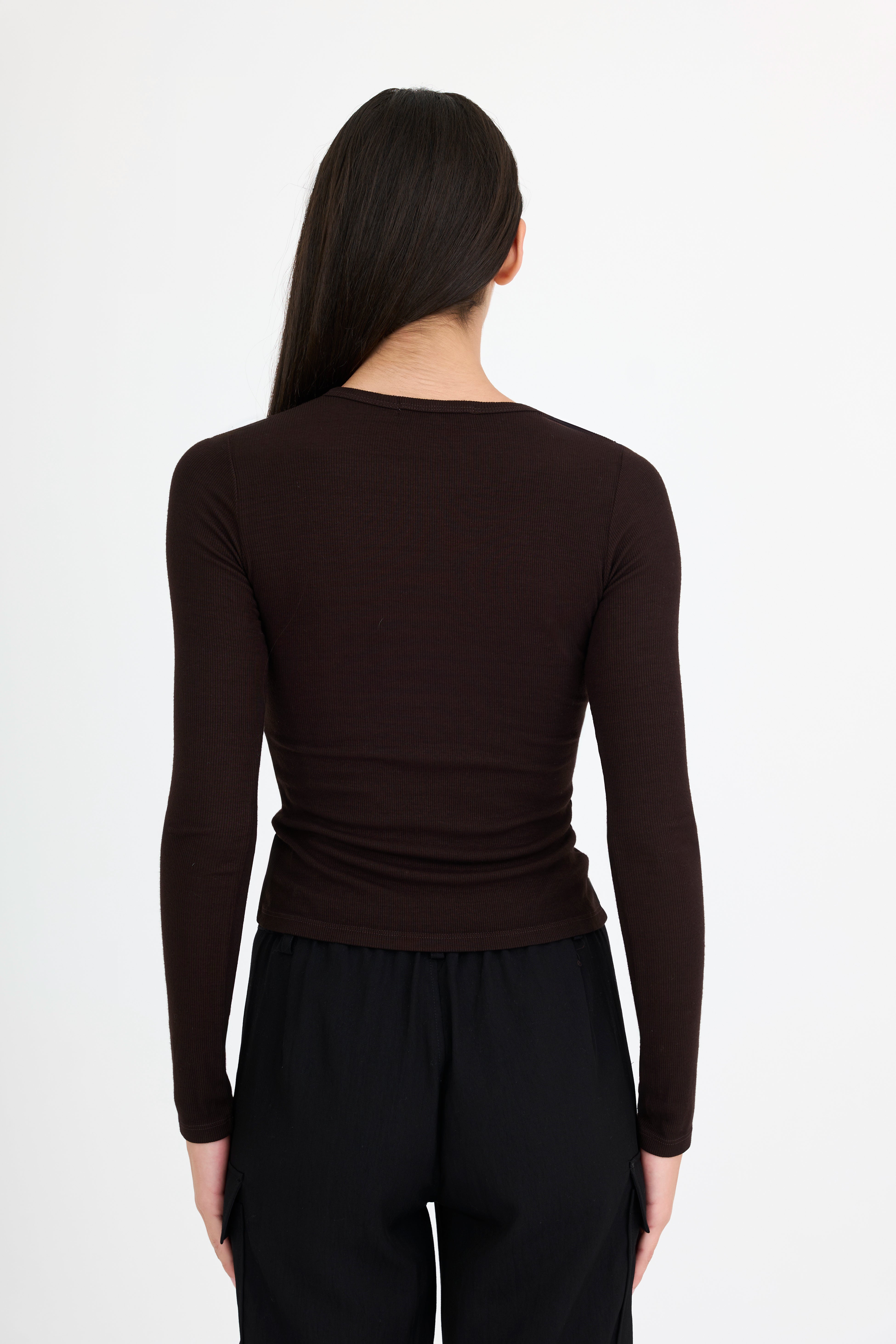 Woman wearing a brown long-sleeve t-shirt and black pants on a white background