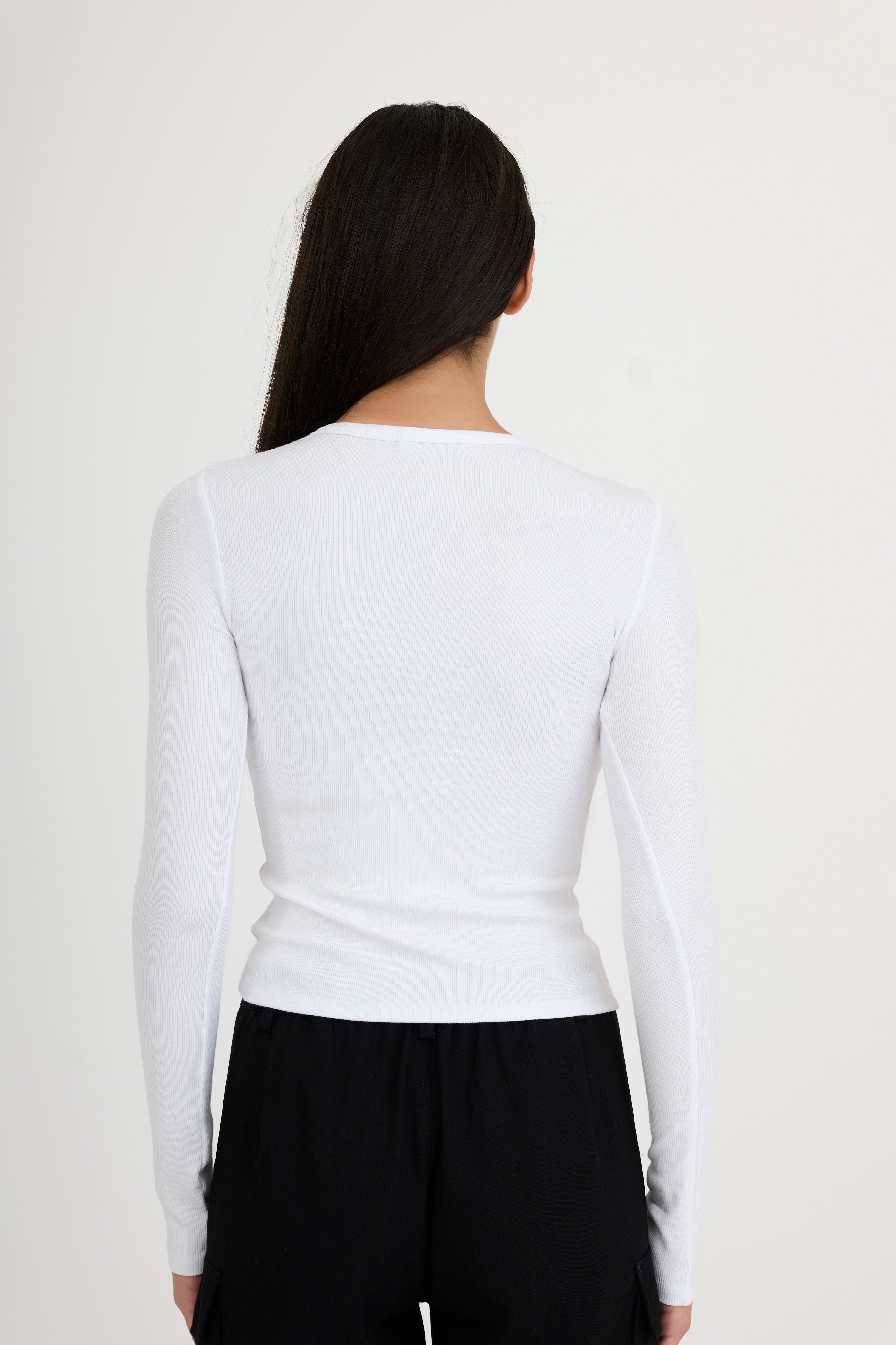 Woman wearing a white long-sleeve t-shirt and black pants on a white background