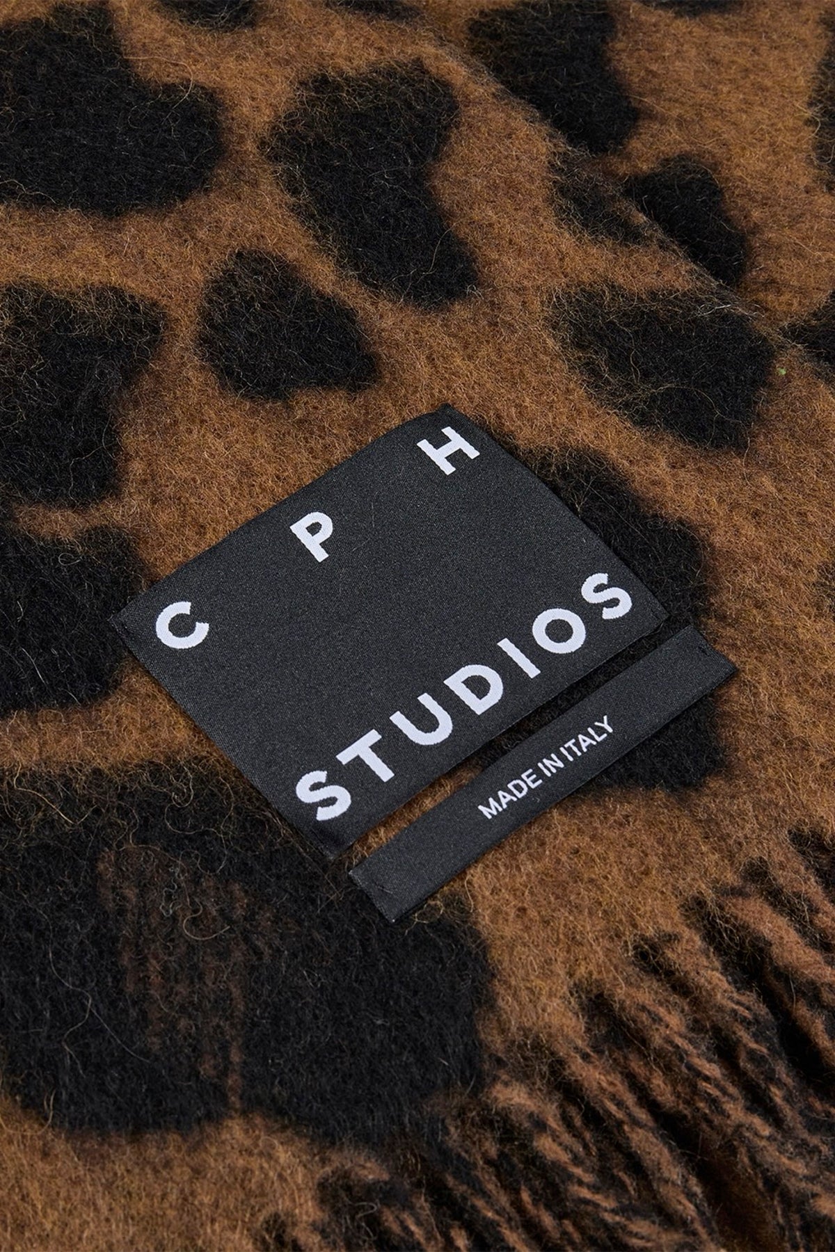 Close-up of a leopard-print shawl with a black fabric tag reading 'CPH STUDIOS' and 'MADE IN ITALY'.
