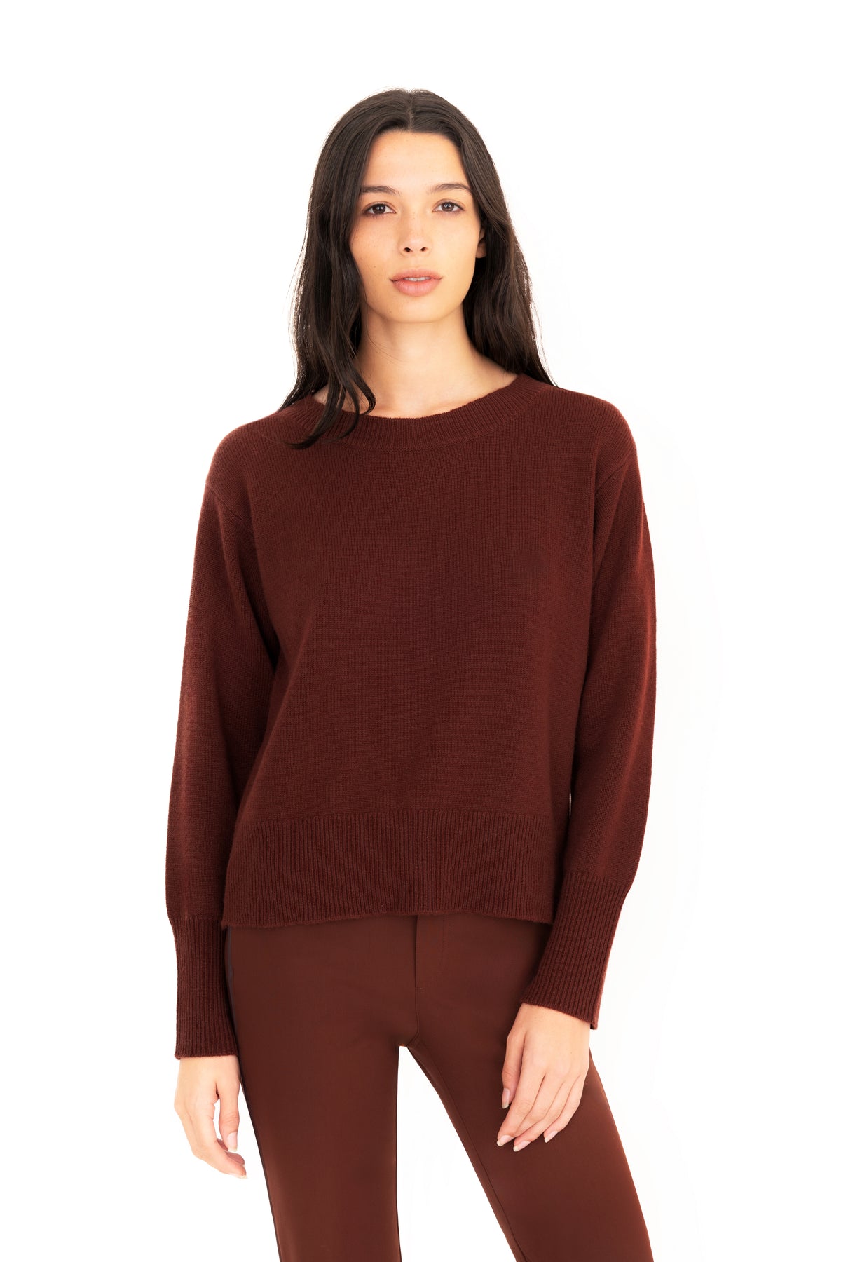 A woman modeling a dark brown crewneck knit sweater and matching brown pants against a plain white background.