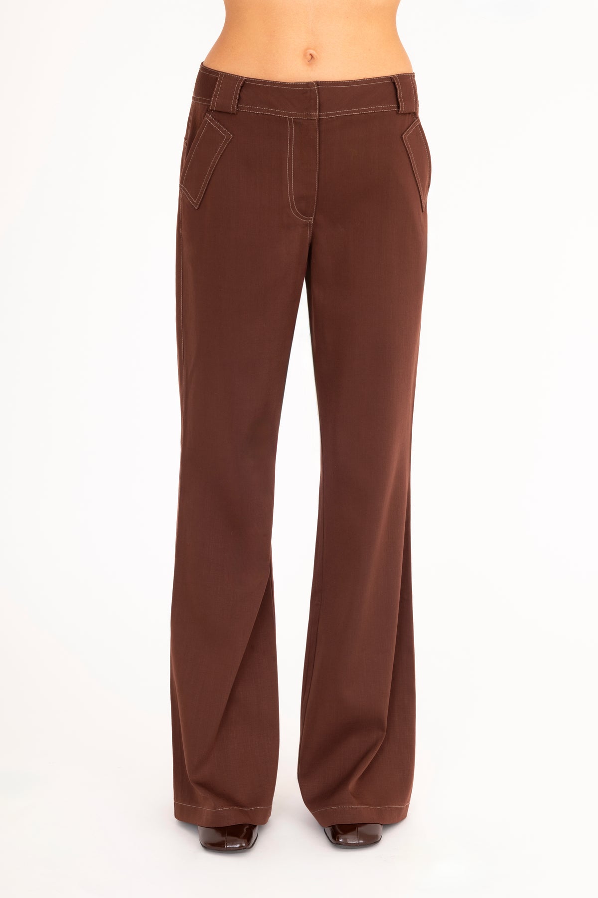 A woman wearing brown wide-leg pants, shown from the waist down against a plain white studio background.