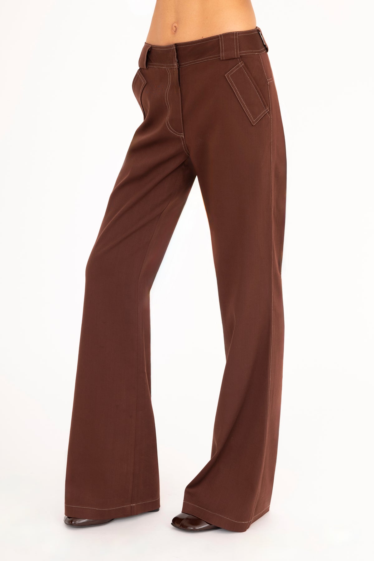 A woman wearing brown wide-leg pants, shown from the waist down against a plain white studio background.