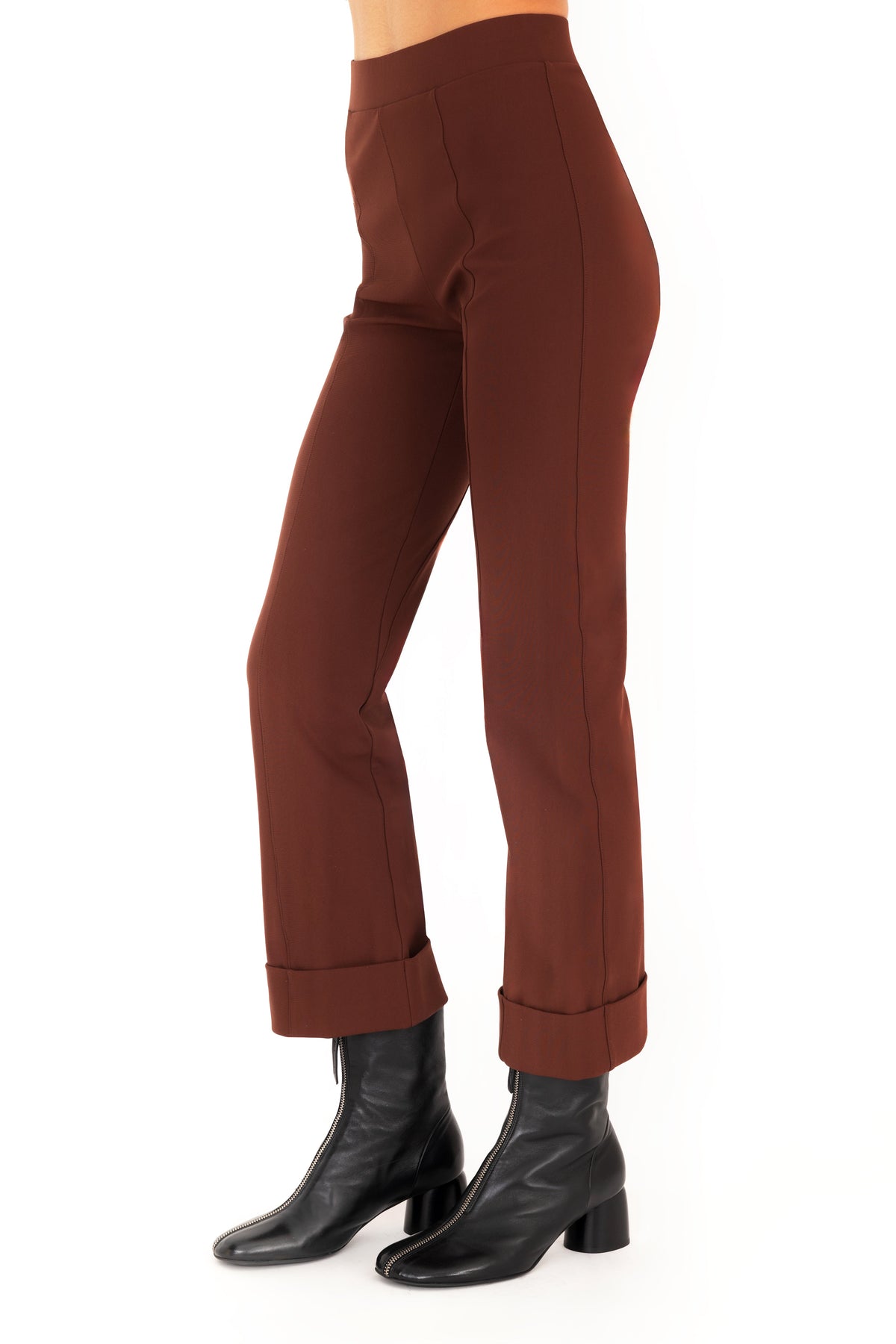 A model wearing dark brown cropped pants with rolled cuffs and black ankle boots, shown from the waist down on a white studio background.