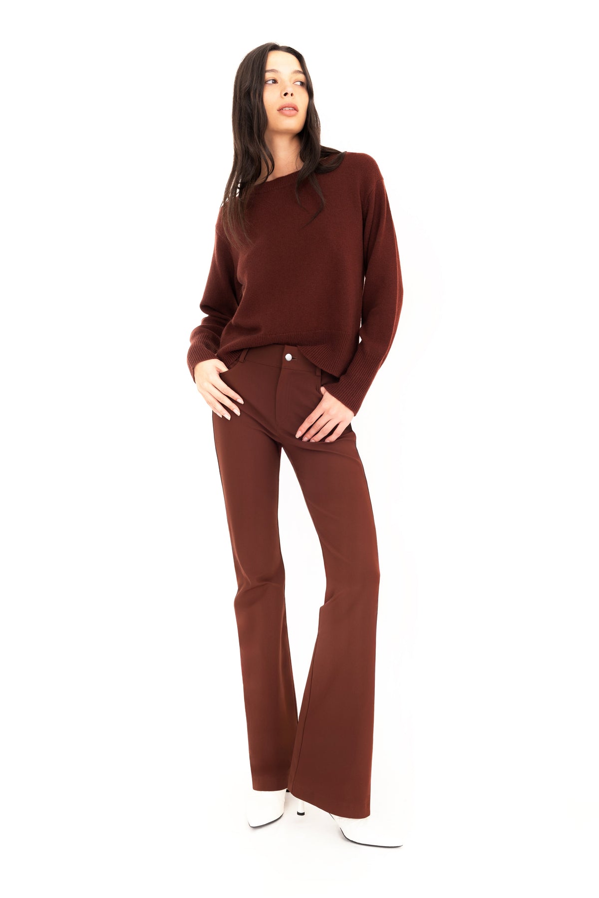 Woman wearing brown cashmere sweater and flare jean pants against a white studio background.