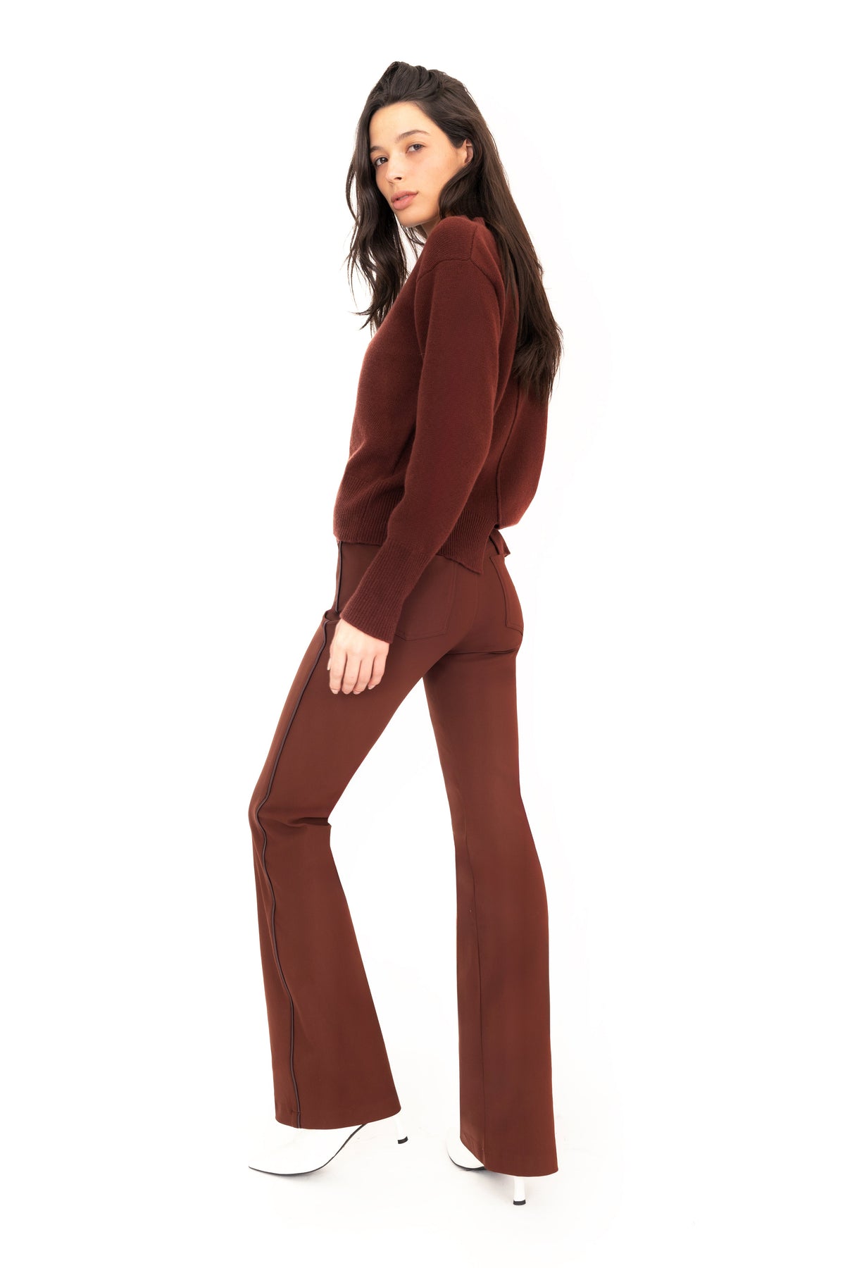 Woman wearing brown cashmere sweater and flare jean pants against a white studio background.