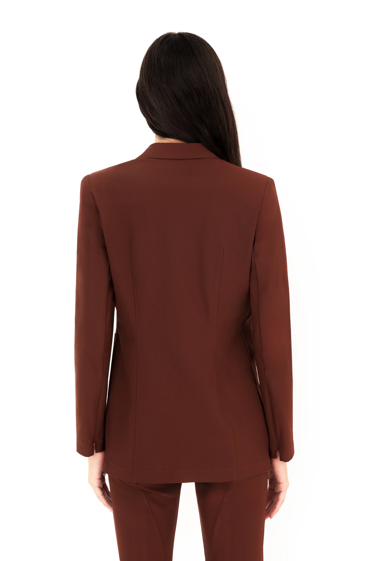 A woman viewed from the back wearing a tailored brown blazer with matching trousers against a plain white studio background.