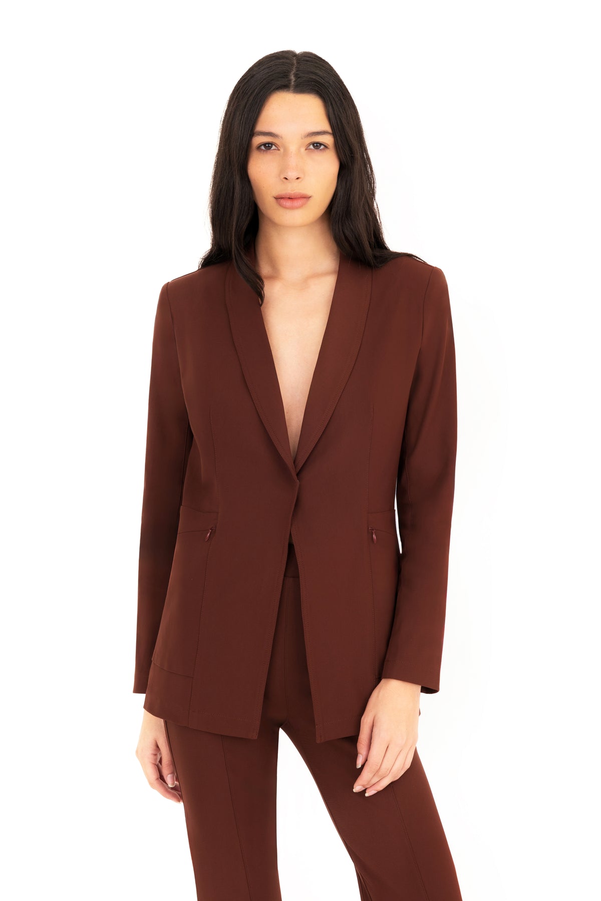 A woman modeling a matching brown tailored blazer and trousers set against a plain white studio background.