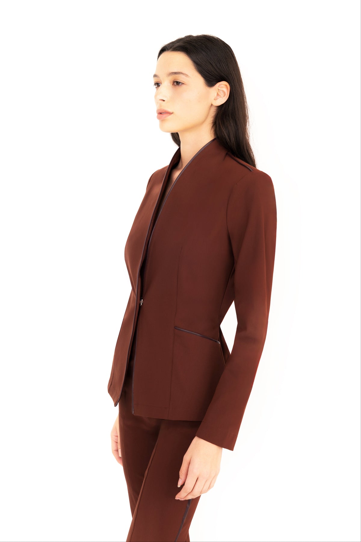 A woman modeling a matching brown structured blazer and trousers set against a plain white background.