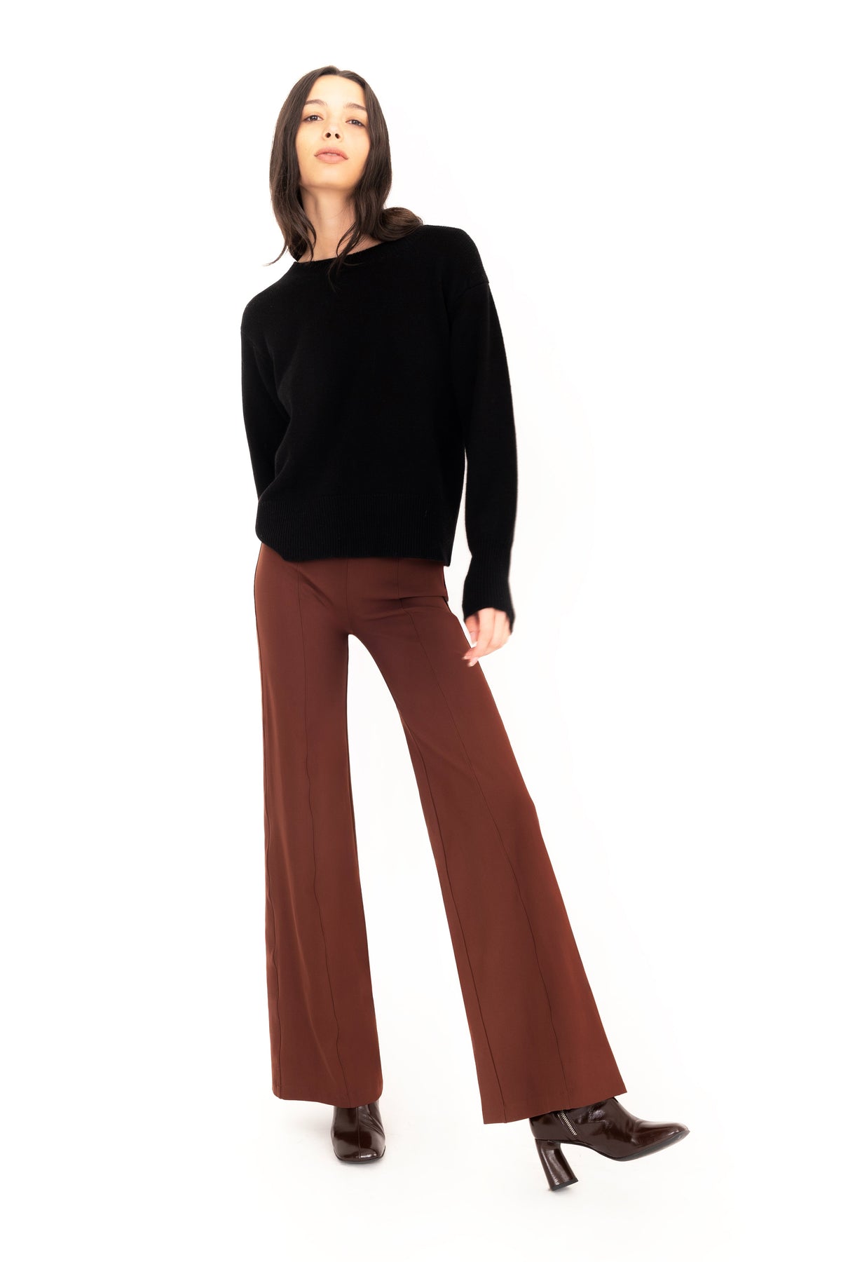 Woman wearing a black cashmere crew-neck sweater and brown wide-leg pants on a white background.