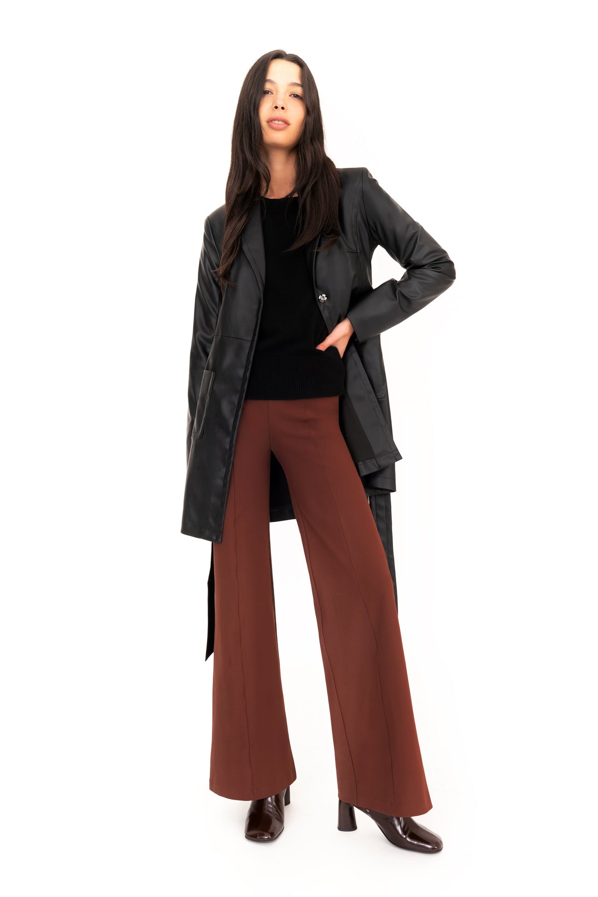 Woman wearing a black vegan leather trench coat, black cashmere sweater and brown wide-leg pants on a white background.