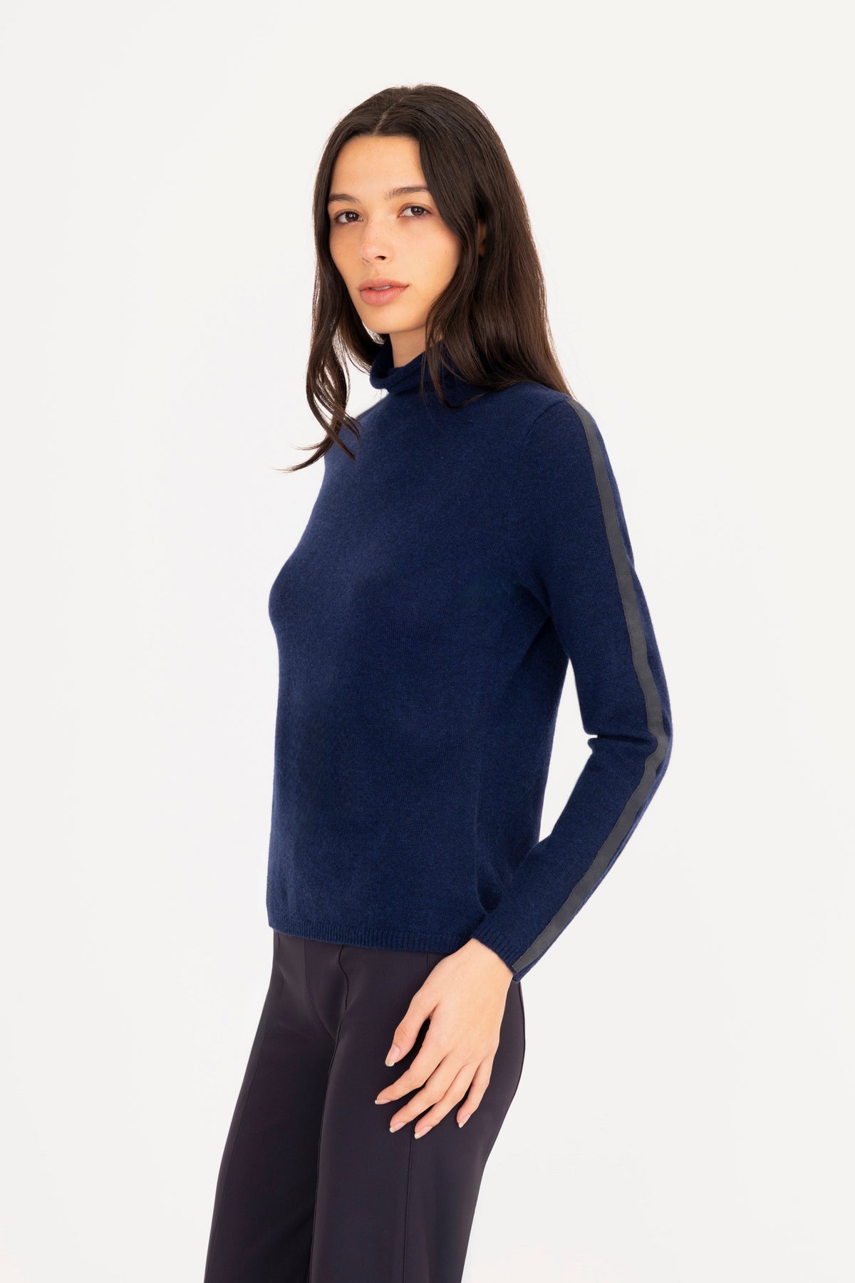A woman modeling a navy blue mock neck knit sweater, paired with navy blue trousers, against a plain white studio background.