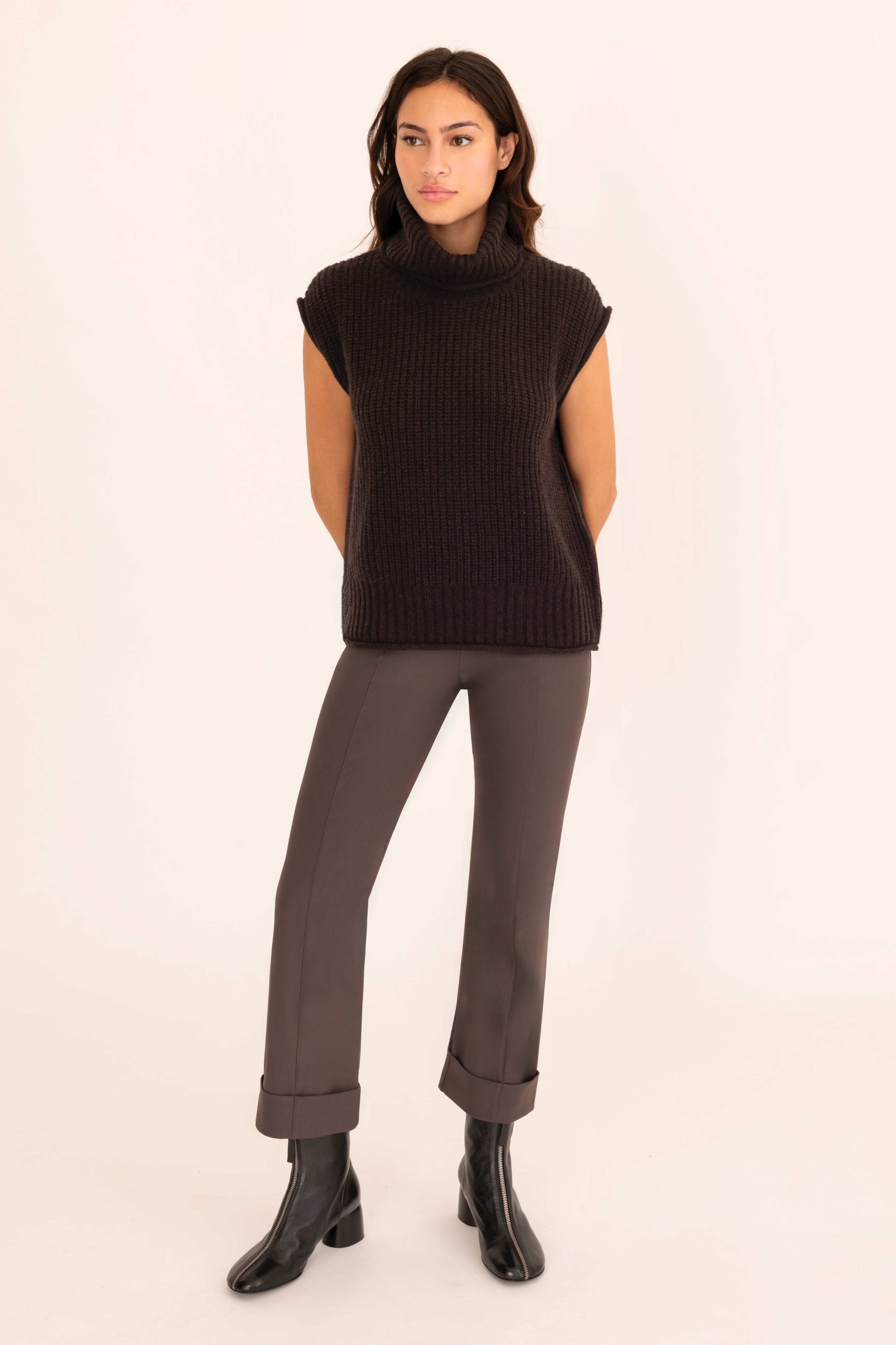 Woman wearing a brown sleeveless sweater and pants on a beige background