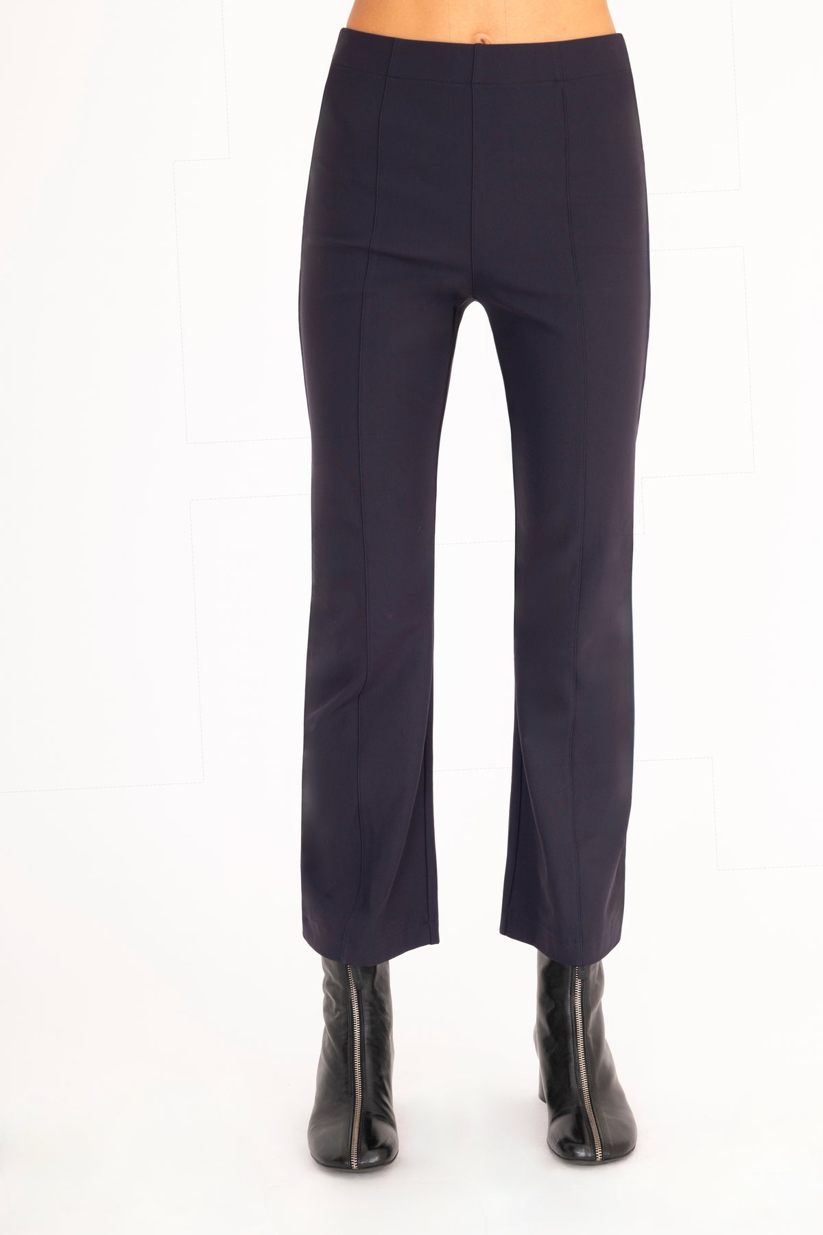 A front view of a model wearing dark blue flared pants with dark blue vegan leather contrast piping and black leather ankle boots, set against a plain white background.