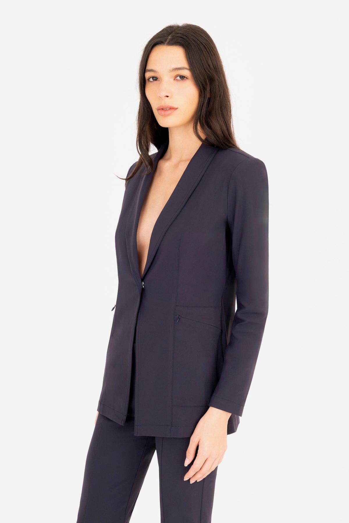 A woman modeling a matching navy blue tailored blazer and trousers set against a plain white studio background.