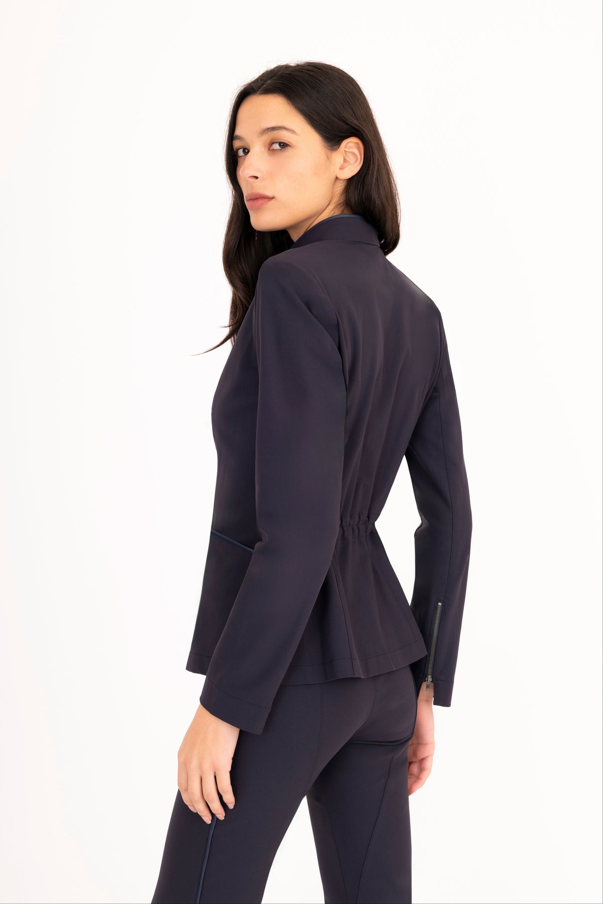 A woman modeling a dark navy blue tailored blazer and matching trousers against a clean white studio background.