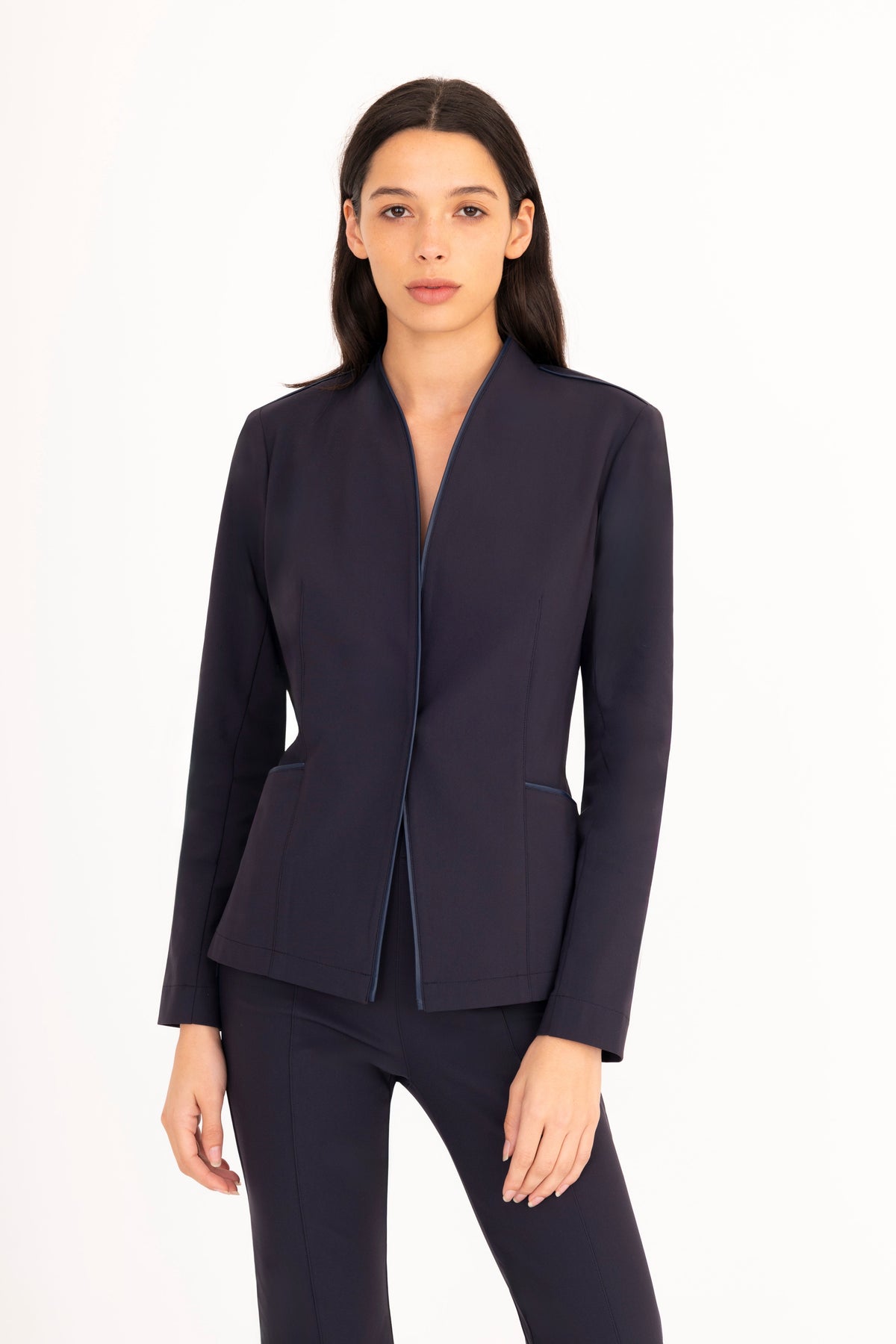 A woman modeling a dark navy blue tailored blazer with matching trousers against a plain white studio background.