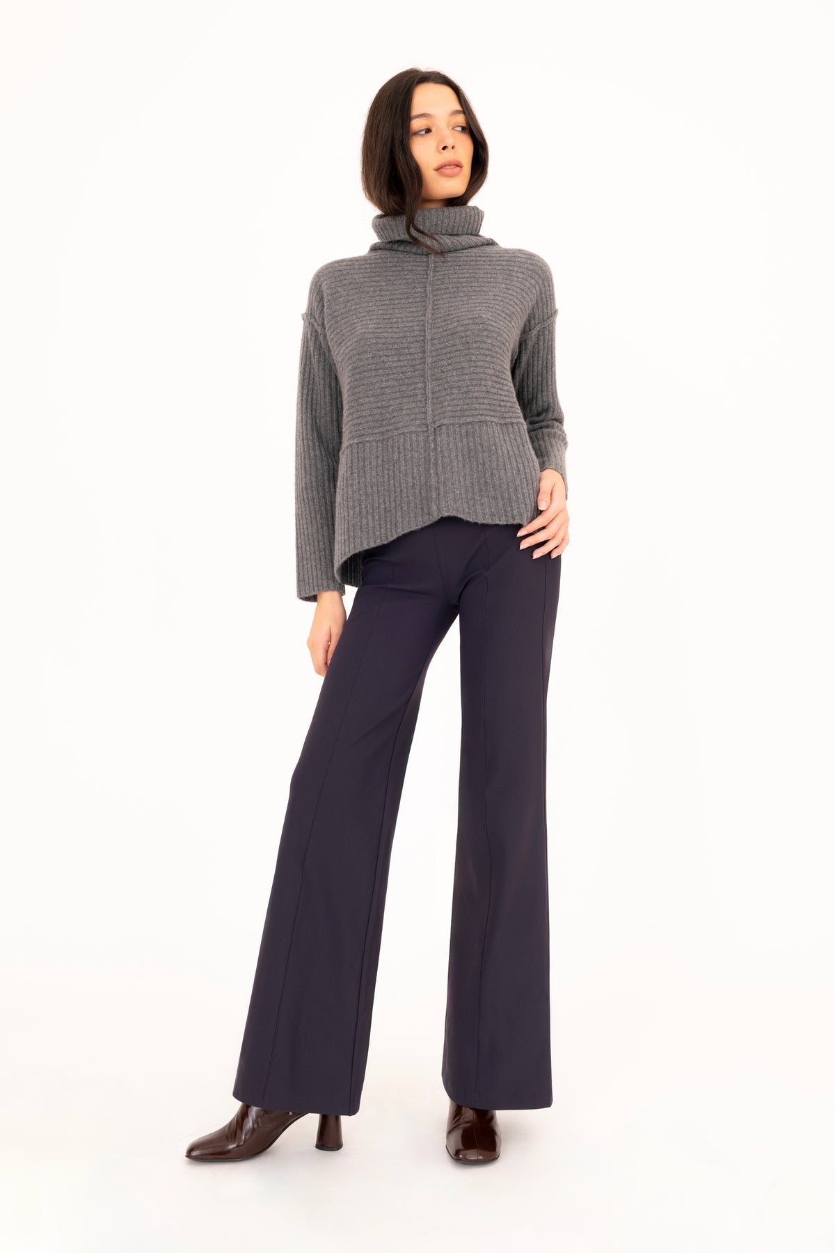 A woman modeling a gray cashmere ribbed turtleneck sweater and dark navy wide-leg trousers against a plain white studio background.