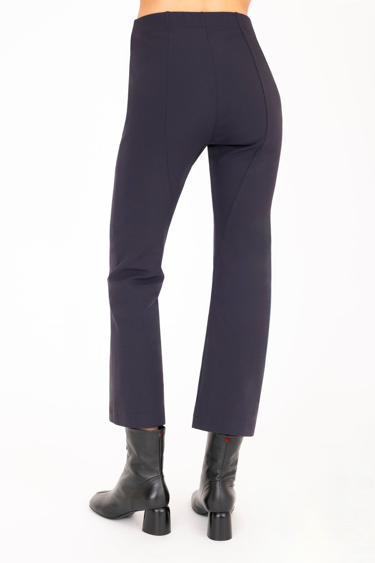 A model shown from behind wearing dark navy cropped pants with side zip pockets and black ankle boots, shown from the waist down on a plain white studio background.