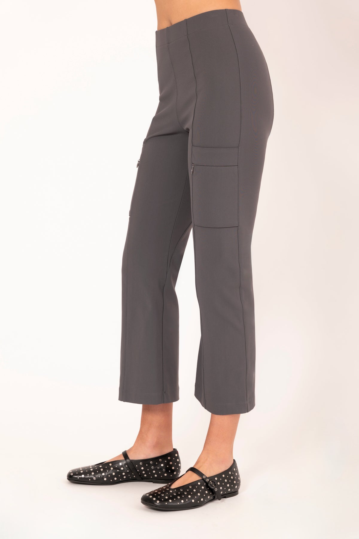 A model shown from the waist down wearing dark gray cropped pants with side cargo pockets and black studded Mary Jane flats, photographed against a plain light background.