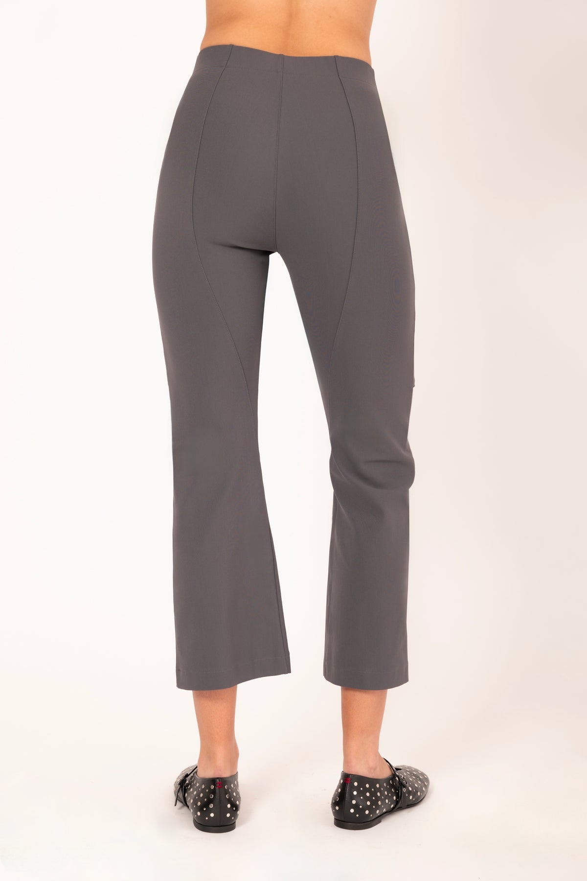 A model shown from the back wearing high-waisted, straight-leg cropped pants in a solid dark gray color, paired with black studded flats, against a plain off-white studio background.