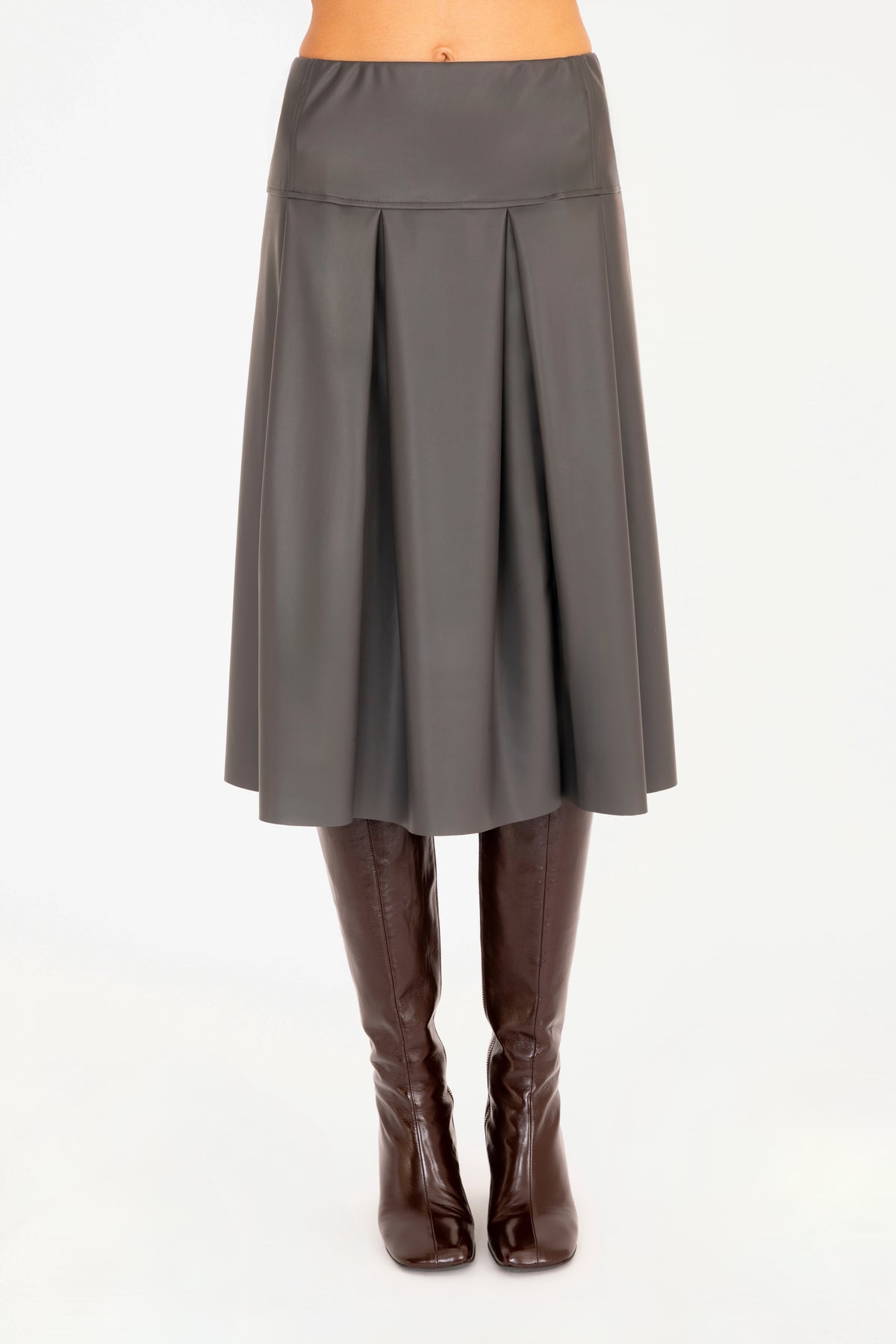 A gray vegan leather pleated A-line skirt shown on a model from the waist down, paired with dark brown knee-high leather boots against a plain white background.