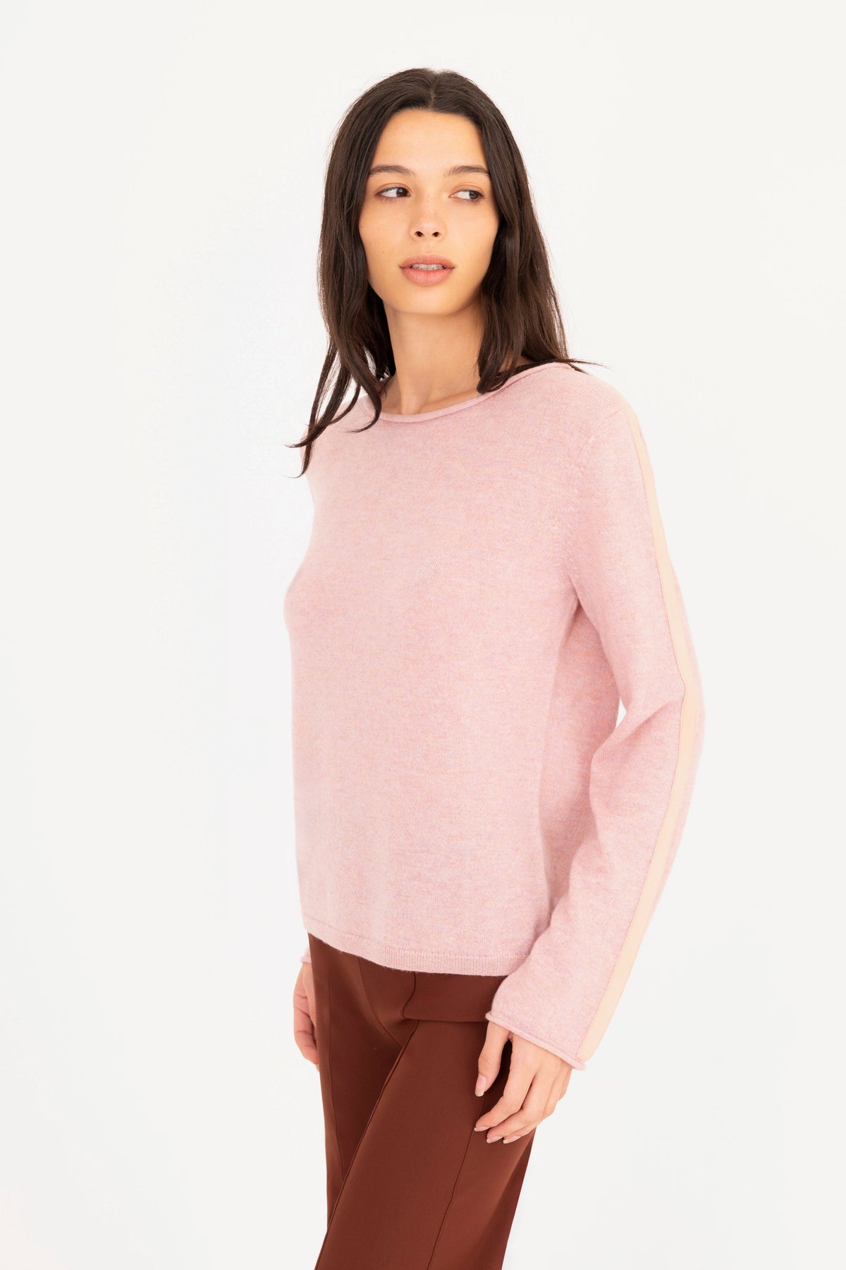 A woman modeling a pink long-sleeve knit sweater, paired with brown pants, against a plain white studio background.