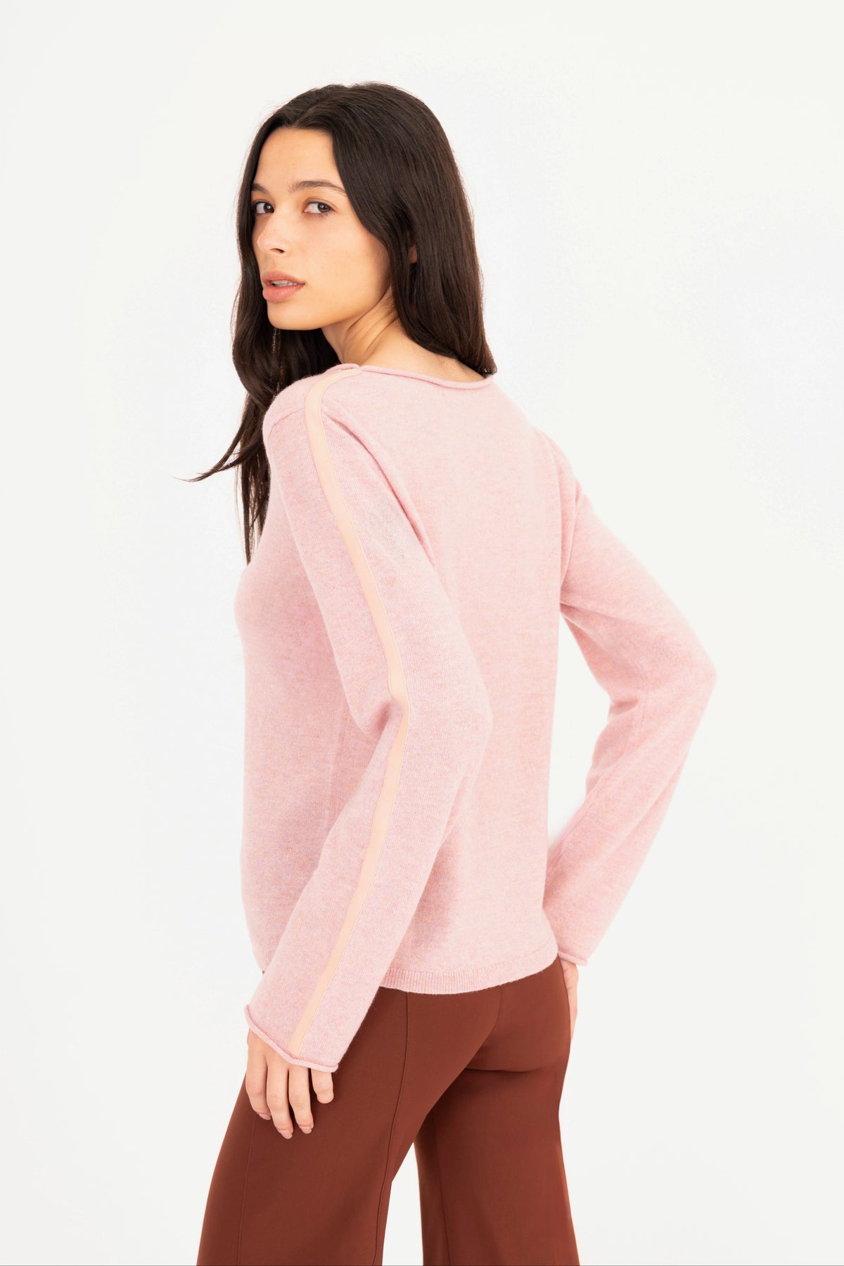 A woman modeling a pink long-sleeve knit sweater, paired with brown pants, against a plain white studio background.