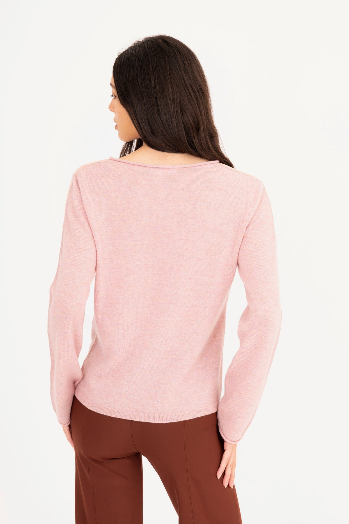A woman modeling a pink long-sleeve knit sweater, paired with brown pants, against a plain white studio background.