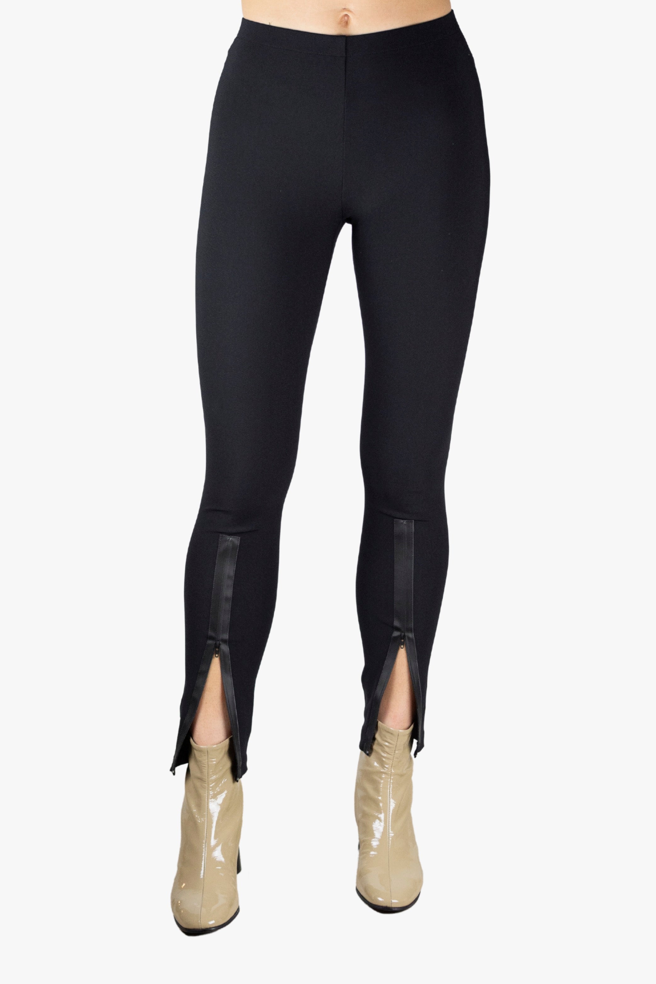 Person wearing black leggings with a slit on a plain background