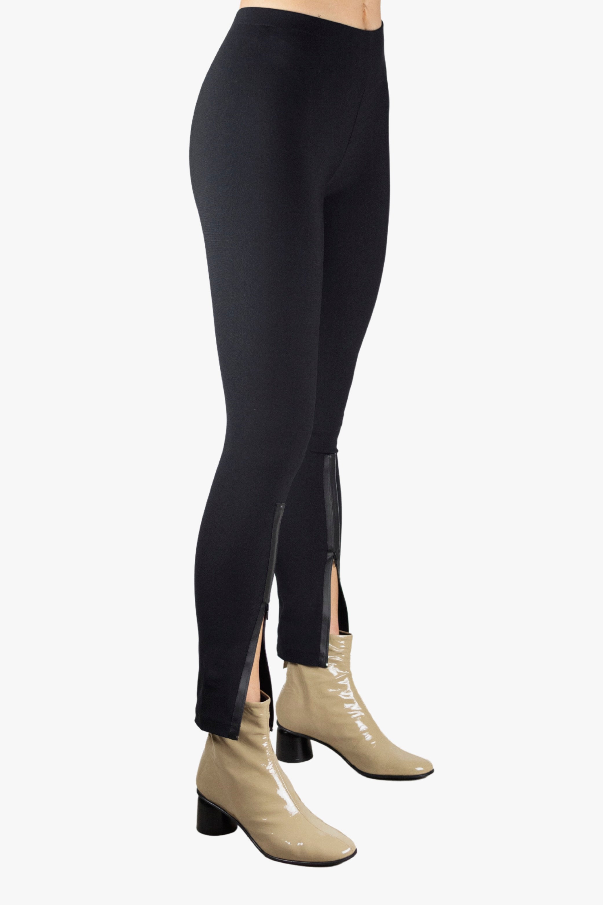 Person wearing black leggings with a slit on a plain background
