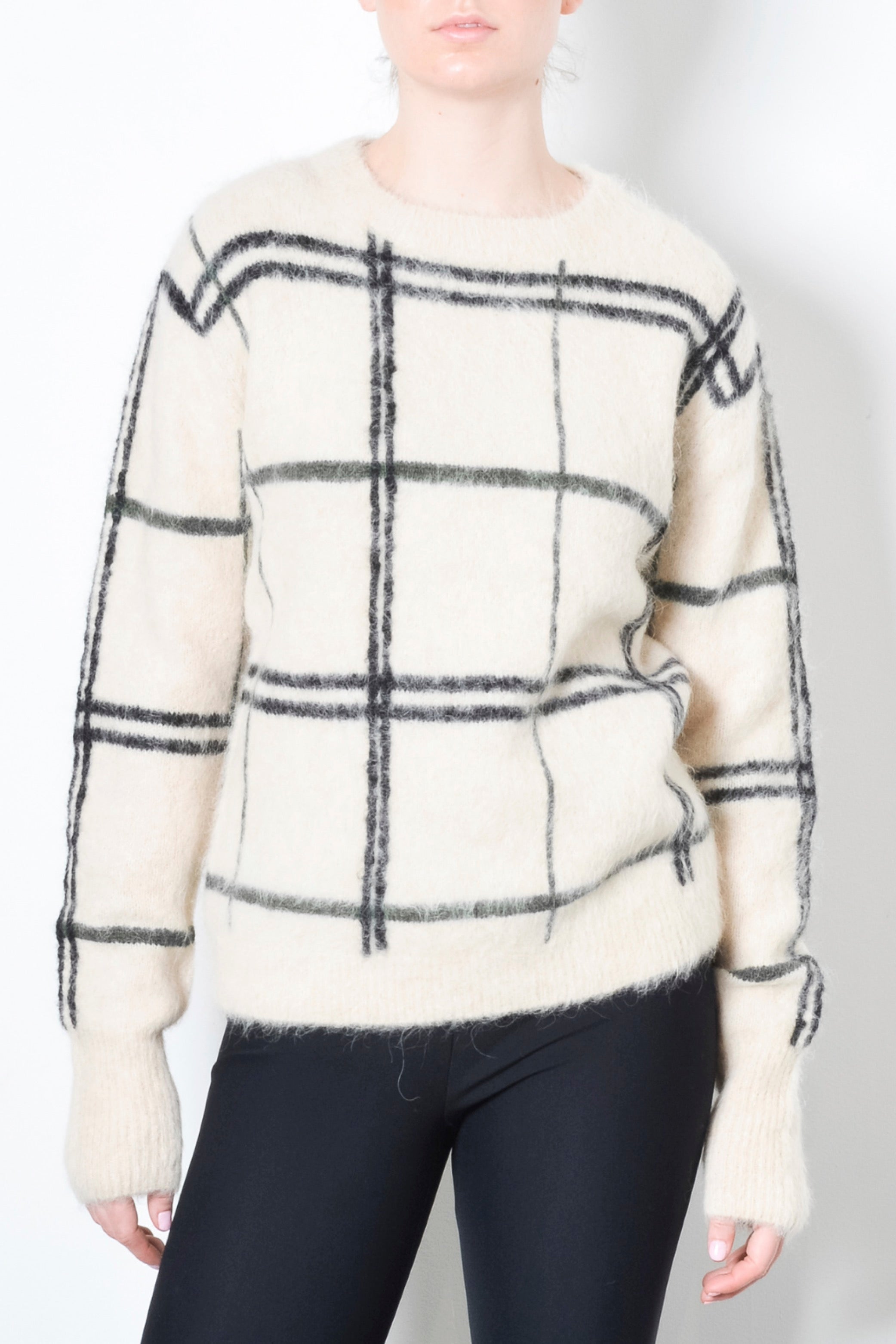 Person wearing a white sweater with black plaid pattern on a plain background