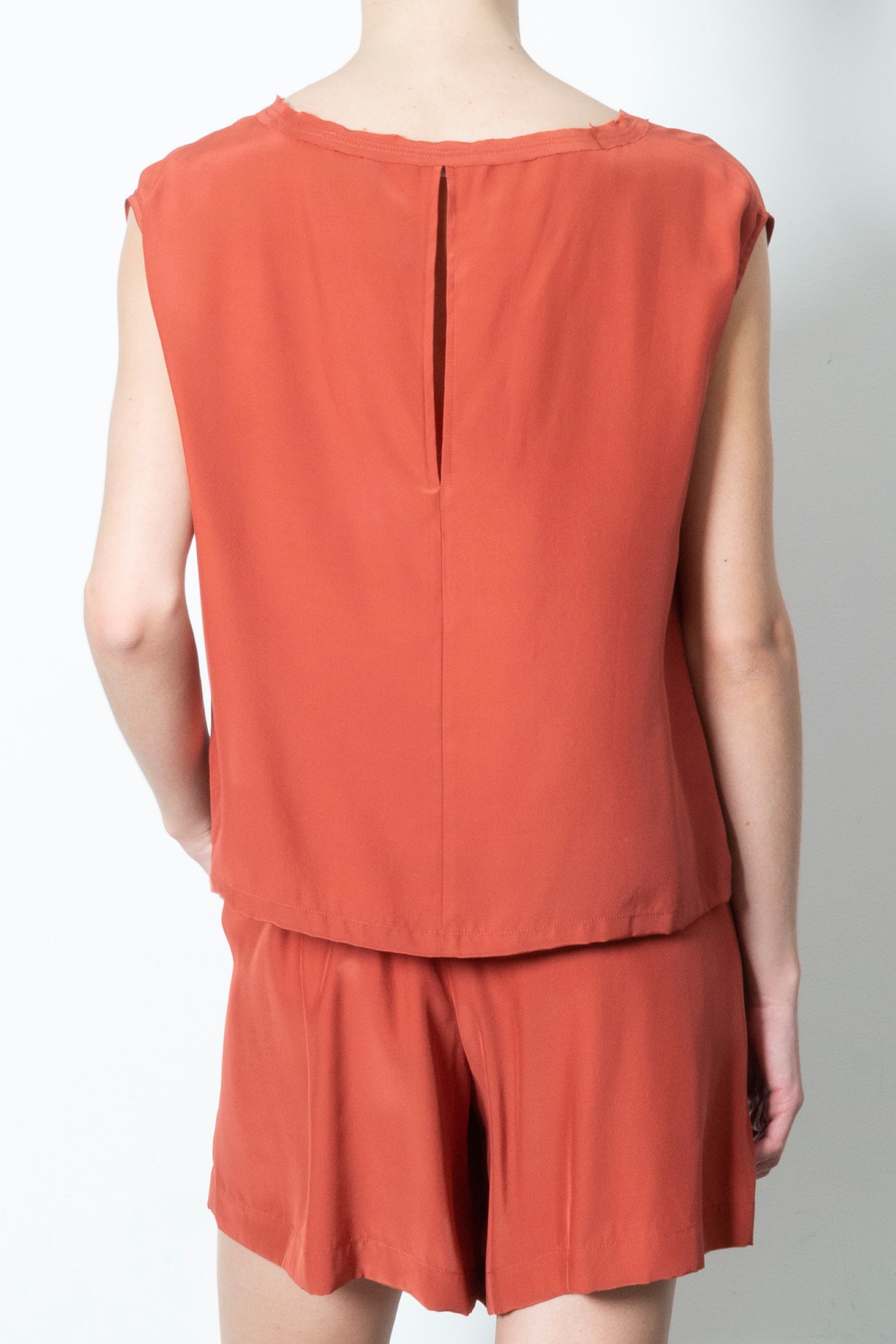 Person wearing a rust-colored sleeveless top and short set on a plain background