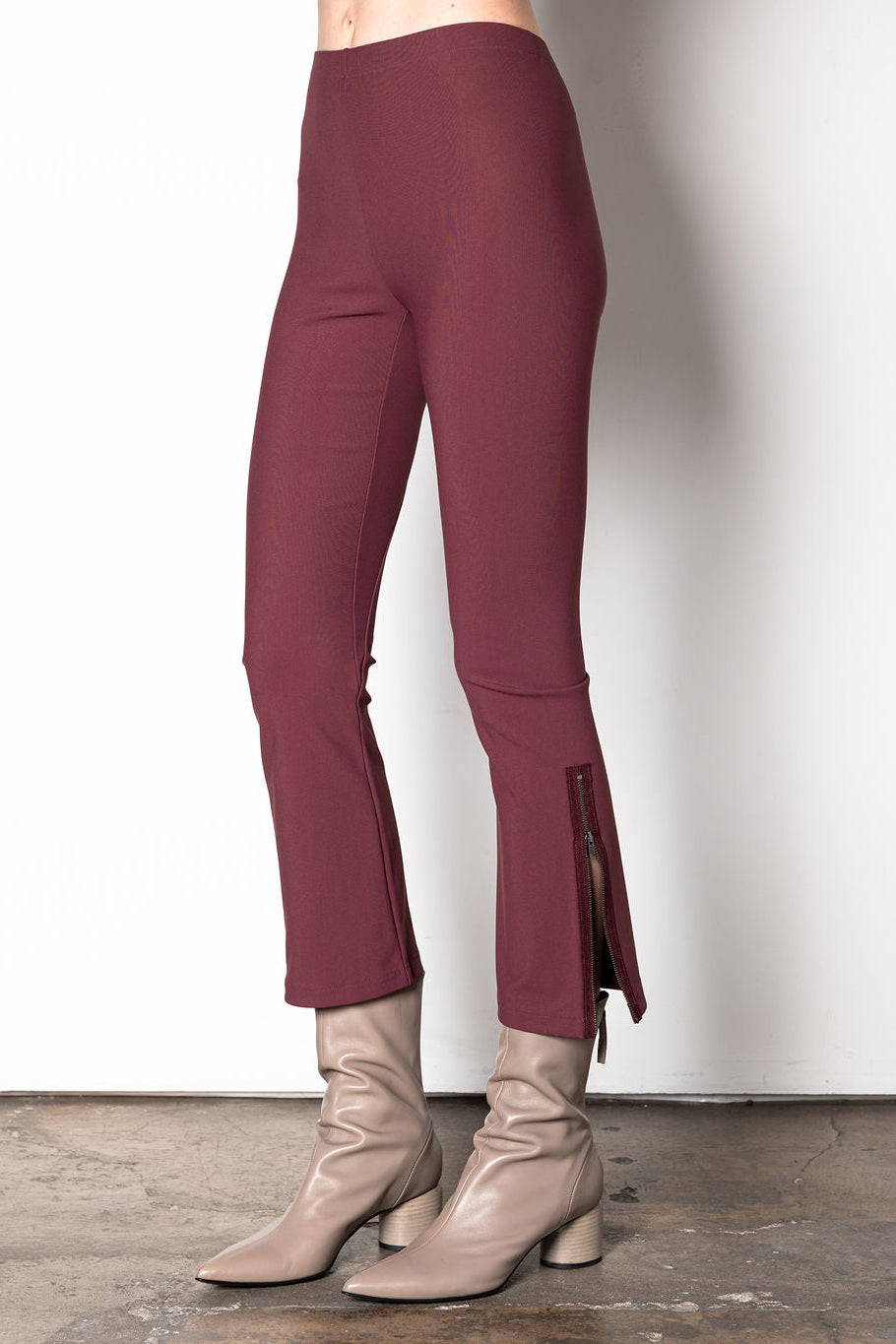 Maroon pants worn with beige boots on a plain background