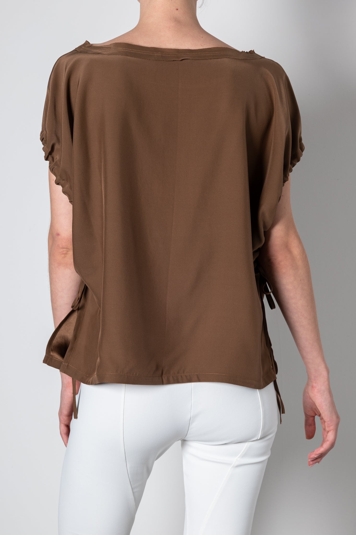 Brown blouse with ruffled sleeves worn by a person on a gray background