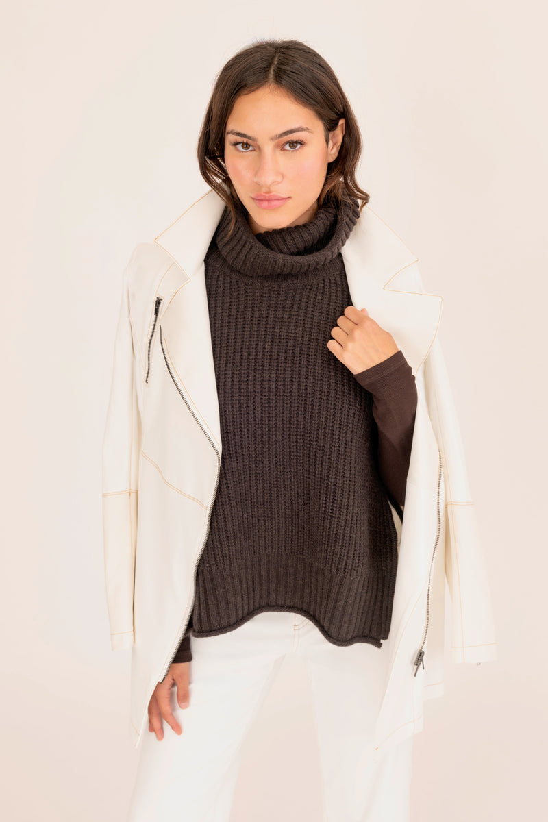 Woman wearing a white coat over a dark sweater and pants on a plain background