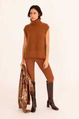 Woman wearing a brown sleeveless sweater, leggings, and boots on a beige background