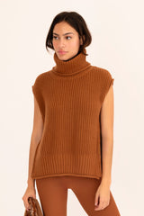 Woman wearing a brown sleeveless sweater, leggings, and boots on a beige background