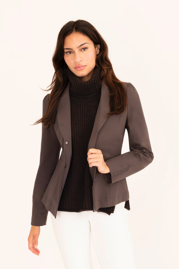 Woman wearing a brown blazer, black top, white pants, and brown shoes on a white background