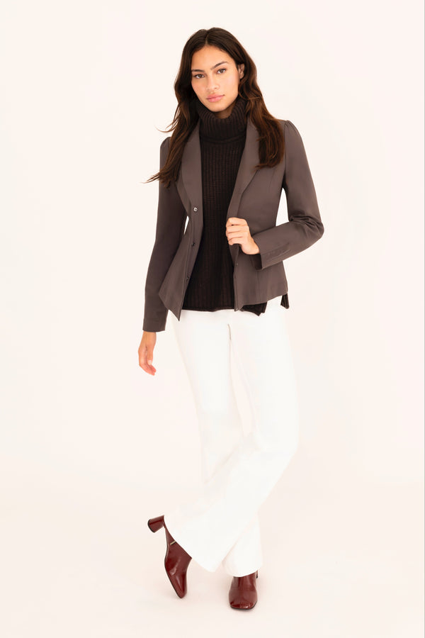 Woman wearing a brown blazer, black top, white pants, and brown shoes on a white background