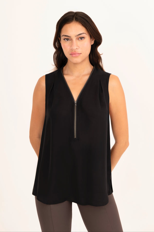 Woman wearing a black sleeveless top with a zipper on a beige background