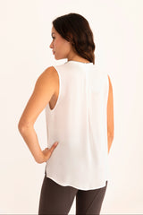 Woman wearing a white sleeveless top and dark pants on a plain background