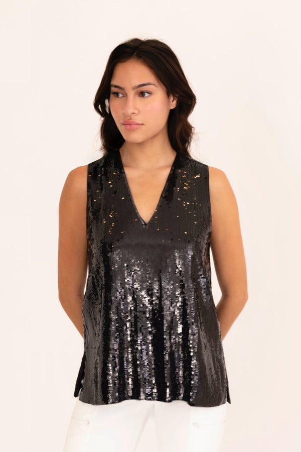 Woman wearing a black sequin top and white pants on a beige background