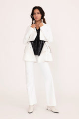 Woman wearing a white suit with a black top on a plain background