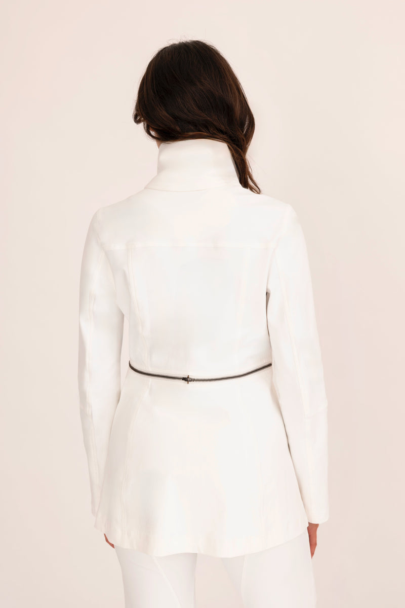 Person wearing a white turtleneck dress with a belt on a light pink background