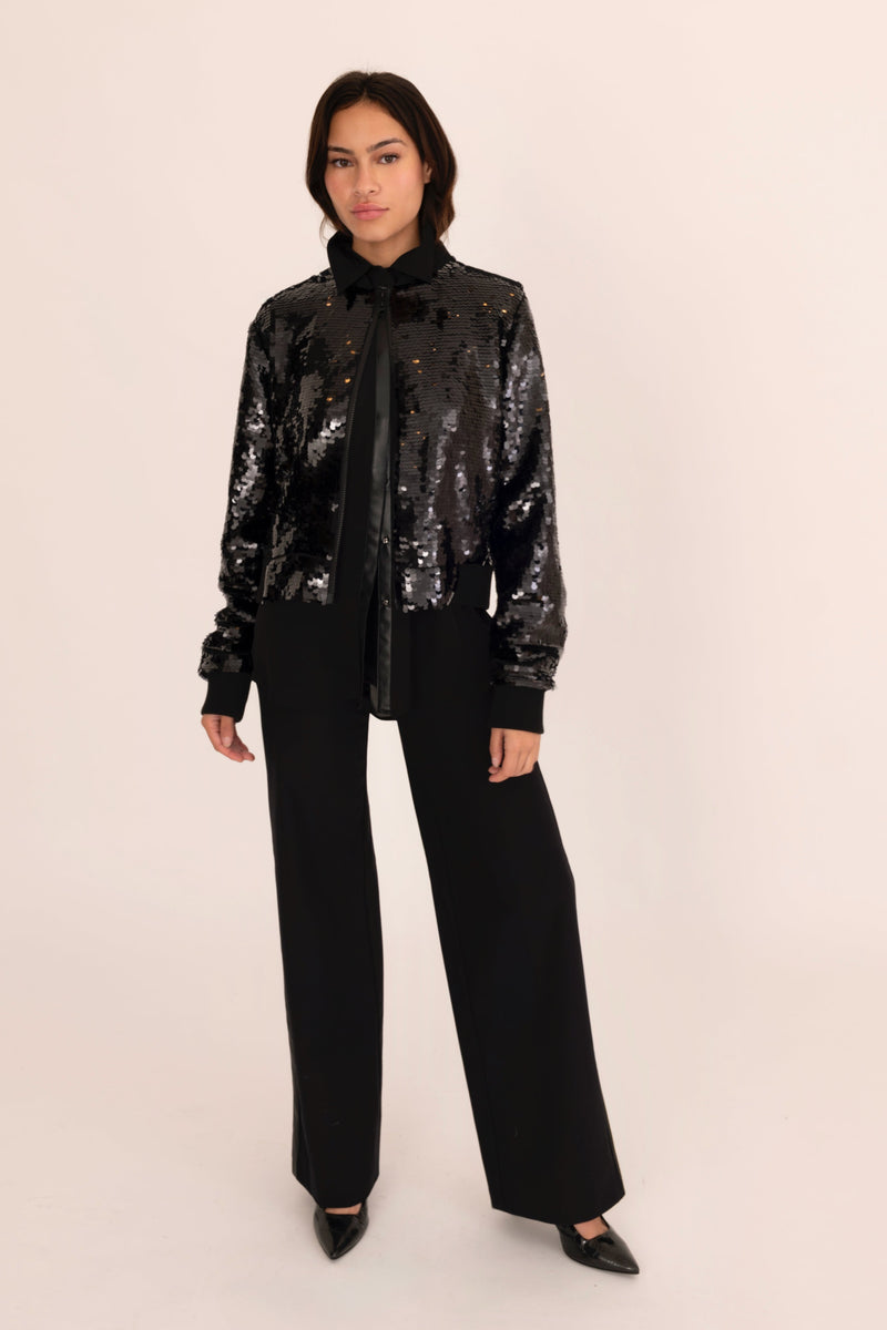 Person wearing a black sequin jacket and pants on a beige background