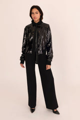 Person wearing a black sequin jacket and pants on a beige background