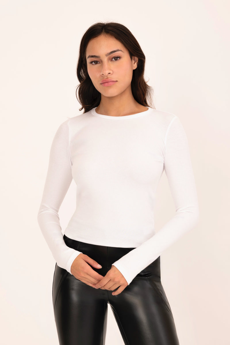 Woman wearing a white long-sleeve top and black leather pants on a beige background