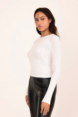 Woman wearing a white long-sleeve top and black leather pants on a plain background